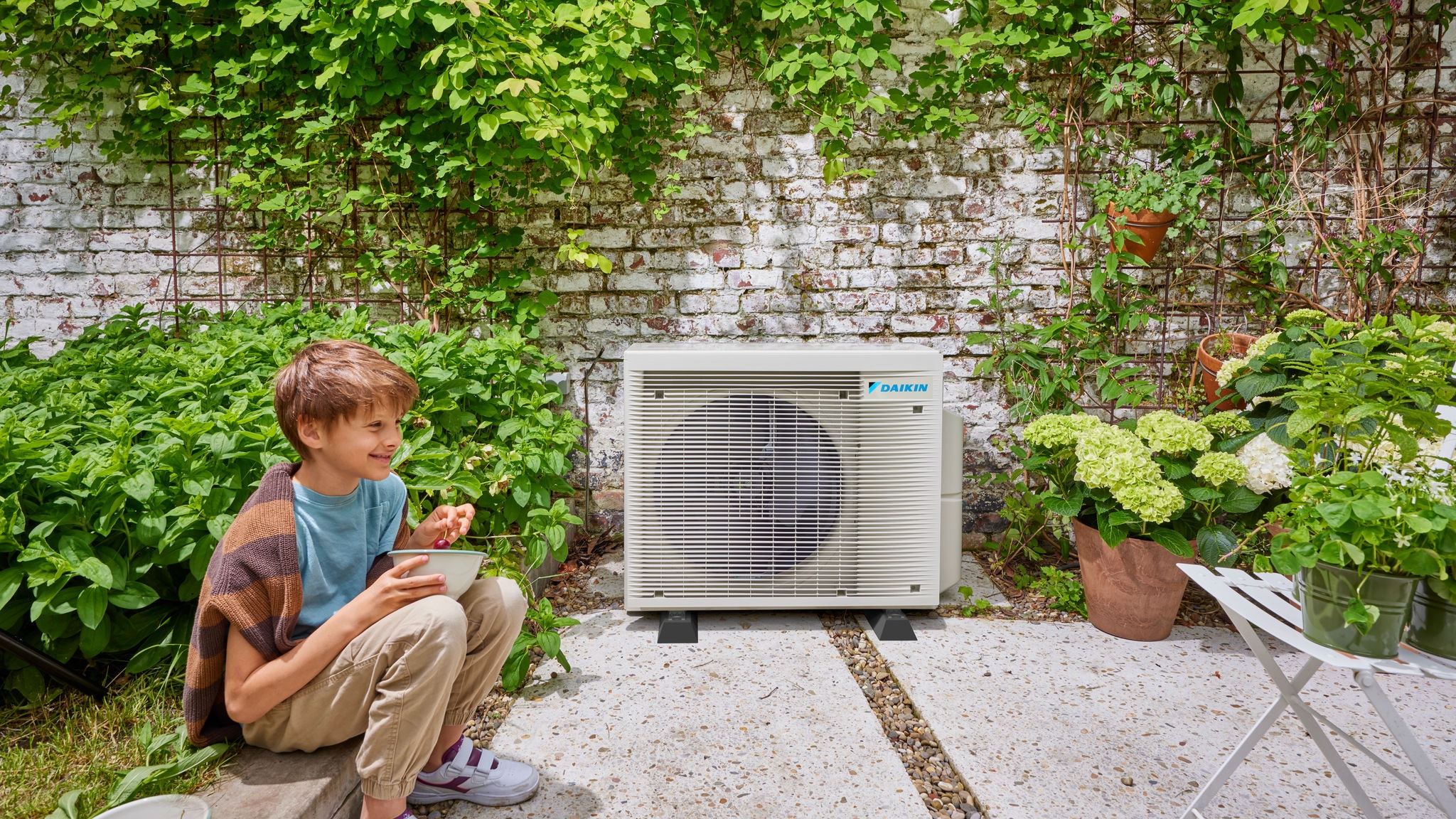 Dijete u blizini vanjske jedinice Daikin hibridne toplotne pumpe, koja spaja energetsku efikasnost i lijepo okruženje u vrtu