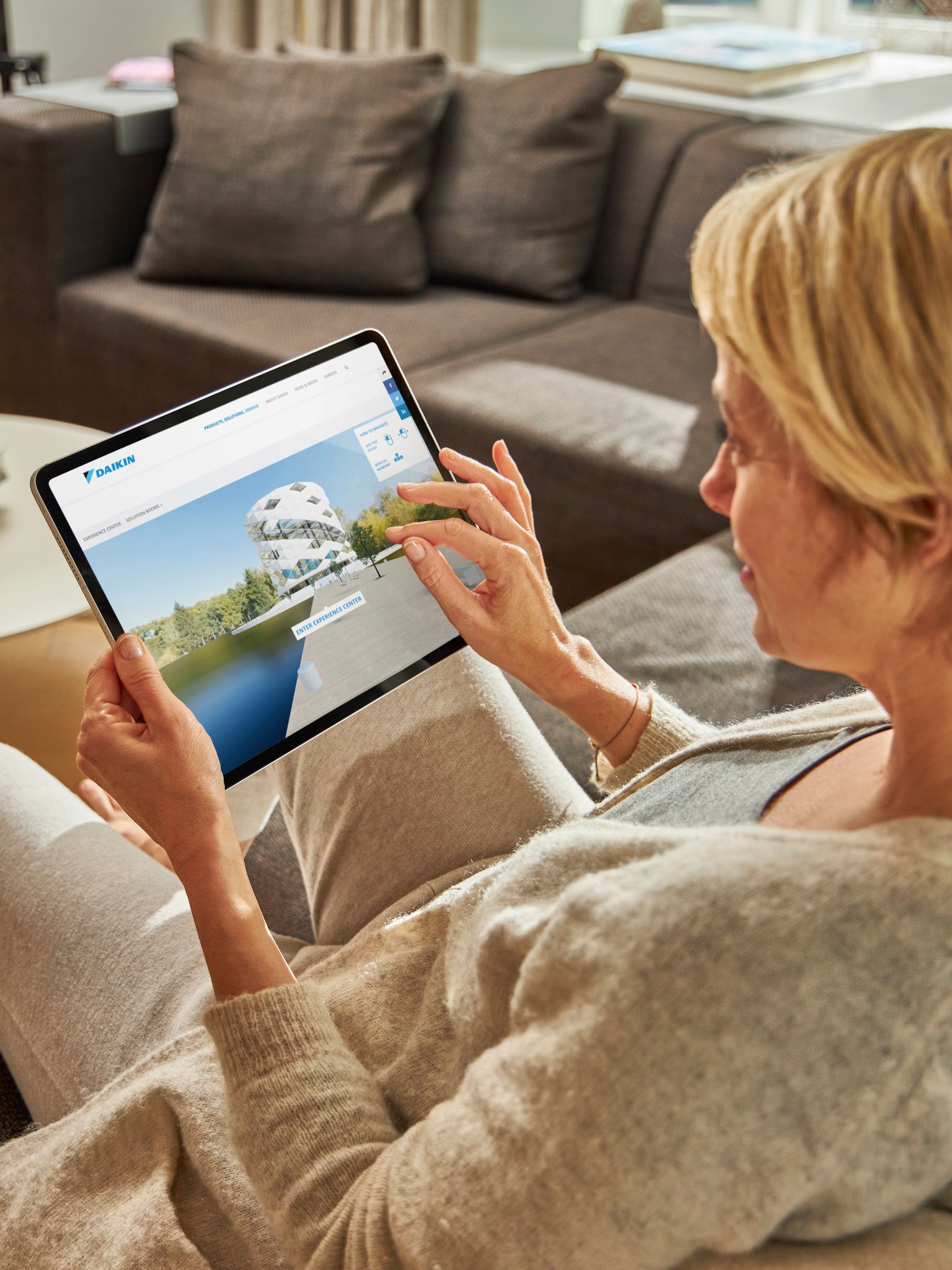 Žena sjedi na kauču i na tablet uređaju pretražuje klima-uređaje u Virtuelnom Experience Centru