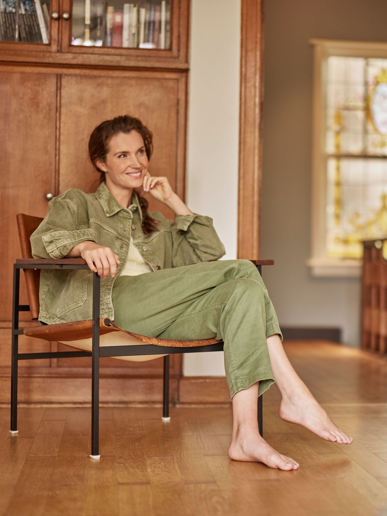 Žena sjedi u svojoj fotelji, bosa, smiješi se i gleda ispred sebe