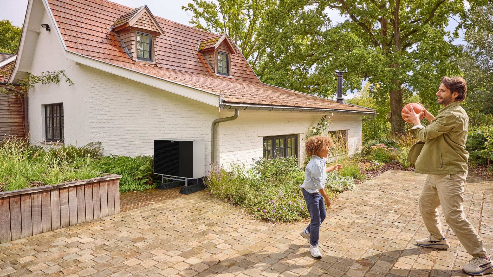 Otac se igra loptom sa svojim djetetom u dvorištu, sa toplotnom pumpom instaliranom u blizini